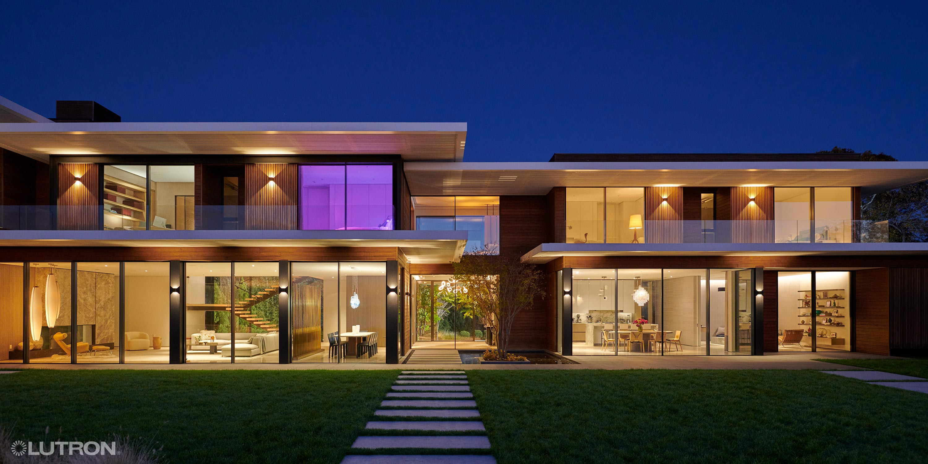 Two-story modern home with large glass walls and warm exterior lighting