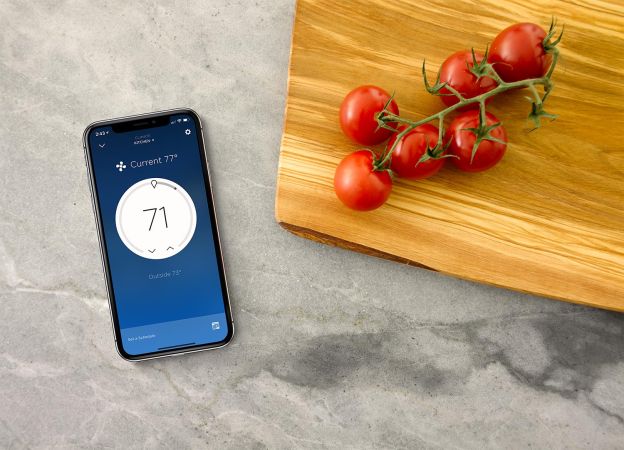 Smartphone showing a climate control screen next to tomatoes on a cutting board