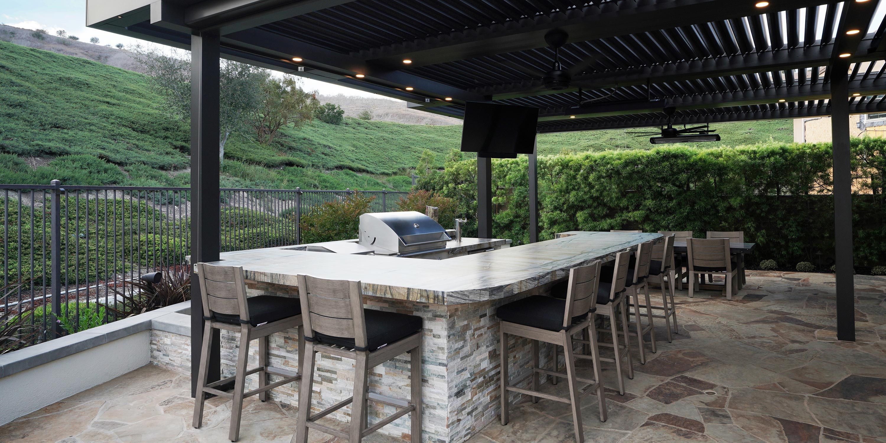 Outdoor kitchen with bar seating, built-in grill, and louvered pergola